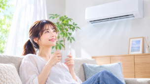明るいリビングでエアコンを使って快適に過ごす女性のイメージ